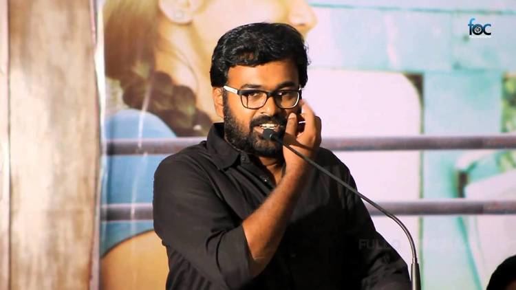 Karu Pazhaniappan giving a speech and hand on his face while wearing eyeglasses and black long sleeves