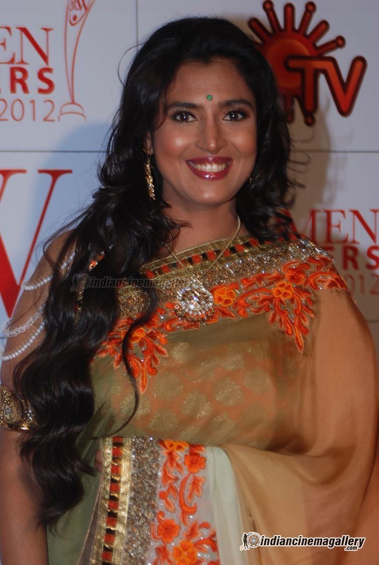 Kasthuri smiling while wearing a brown and orange dress, earrings, and necklace