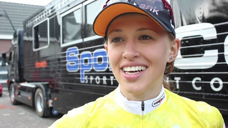 Katarzyna Niewiadoma smiling while wearing a black and orange cap and white and yellow jersey