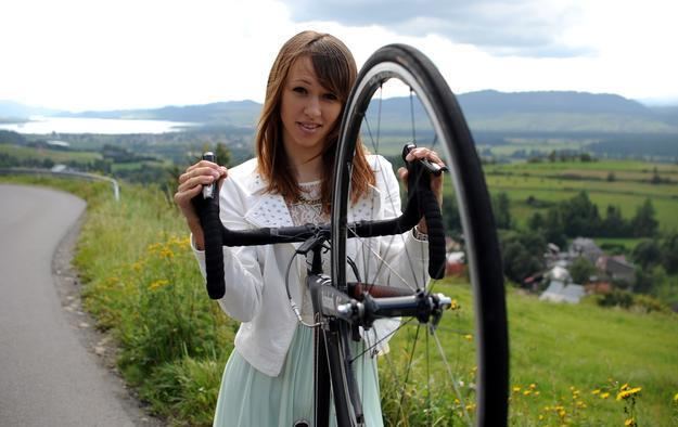 Katarzyna Niewiadoma smiling while holding a bike and wearing a white blazer, white blouse, and light green skirt