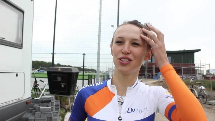 Katarzyna Niewiadoma smiling while fixing her hair and wearing a white, blue, and orange long sleeve jersey