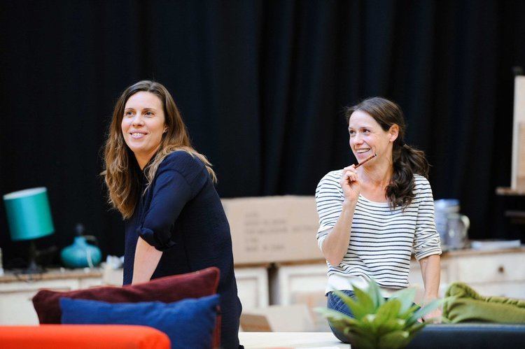 Kate Atkinson smiling while wearing a white and blue striped blouse and a woman beside her is smiling and wearing a black blouse