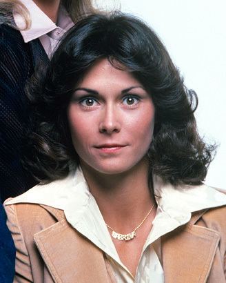 Kate Jackson with a tight-lipped smile while wearing a white blouse, brown blazer, and necklace