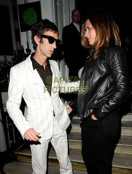 Richard Ashcroft wearing sunglasses, a white striped suit and pants together with his wife Kate Radley wearing a black leather jacket and black pants.