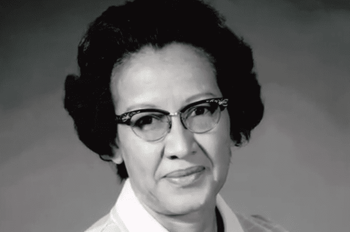 Katherine Johnson with a tight-lipped smile, black short hair, wearing eyeglasses, and a striped top with a white collar.