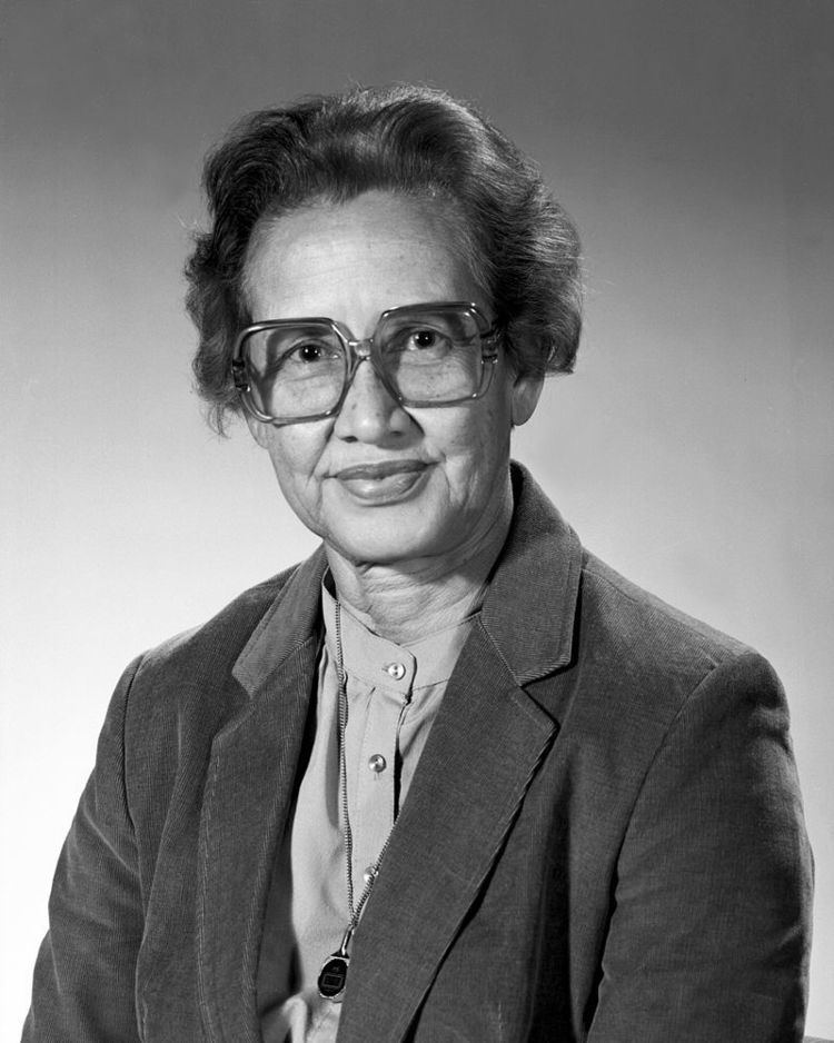 Katherine Johnson with a tight-lipped smile, short hair, wearing eyeglasses, a necklace, and a black blazer over a gray top.