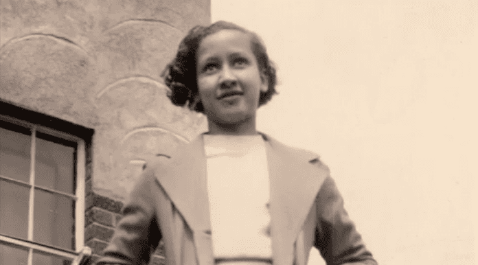 Young Katherine Johnson with a smiling face, curly short hair, wearing a blazer over a white top.
