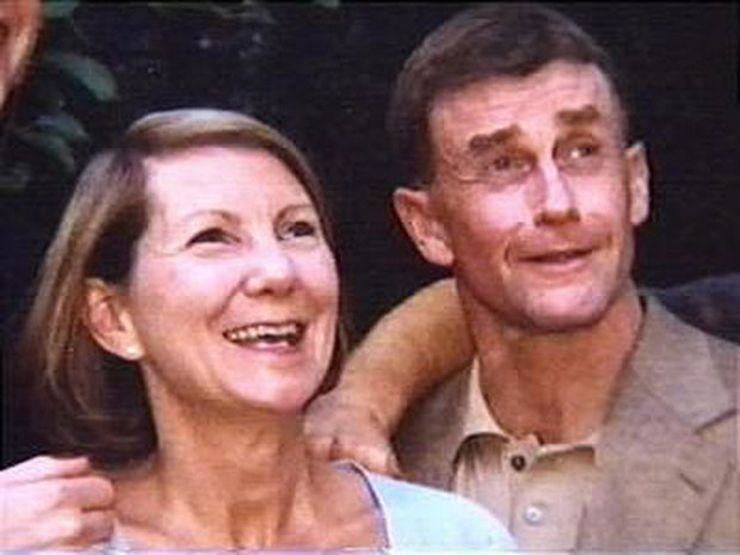 Kathleen Peterson (left) smiling while looking above along with her husband Michael Peterson (right). Kathleen has a short blonde hair wearing a white shirt, and Michael has a black hair and is also smiling while looking above, wearing a brown polo shirt under a brown coat