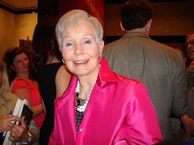 Kim Sullivan Hughes smiling while wearing a pink blazer, inner blouse, and white necklace