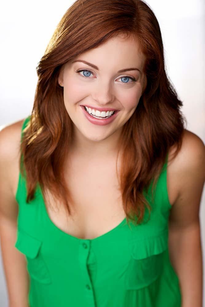 Katie Amis smiling with blue eyes and wavy hair down while wearing a green blouse
