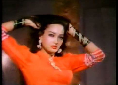 Kaveeta's hands are on her head while wearing an orange blouse, earrings, and bracelet