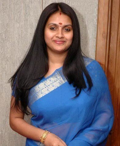 Kaveri smiling while wearing a blue dress and gold necklace