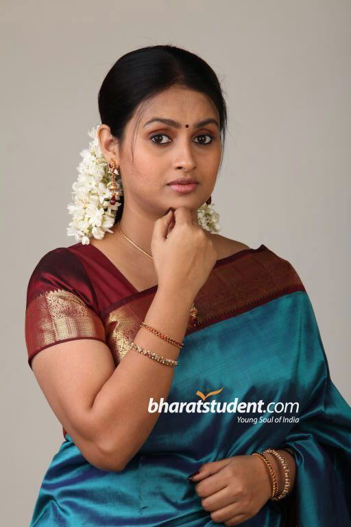 Kaveri's hand on her chin while wearing a maroon and blue dress and some pieces of jewelry