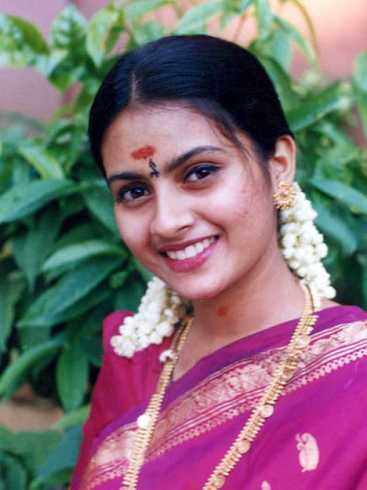 Kaveri smiling while wearing a pink and violet dress, gold earrings, and gold necklace