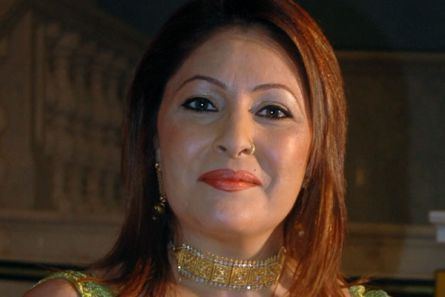Kavita Kapoor smiling closed mouth and wearing a green sleeveless dress and a golden choker along with a nose ring and earrings.