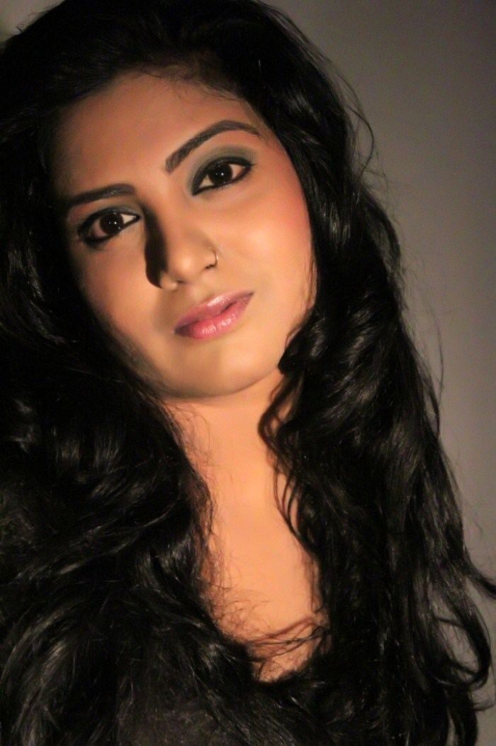 Kavita Radheshyam is serious, has black hair and a nose piercing on her left wing of the nose, and dark-colored eyeshadow.