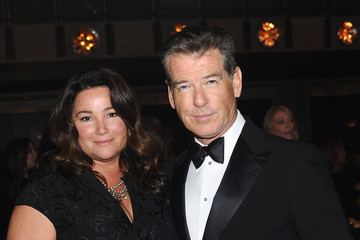Keely Shaye Smith smiling while wearing a black dress and beside him is Pierce Brosnan wearing a black coat, white long sleeves, and bowtie