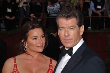 Keely Shaye Smith smiling and wearing a red sleeveless dress while Pierce Brosnan wearing a black coat, white long sleeves, and bowtie