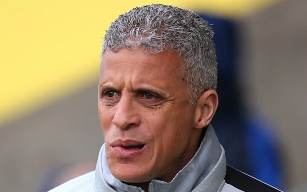 Keith Curle is mad, mouth half open, looking to his right, he has gray hair wearing, a gray jacket with a black line across the shoulder.