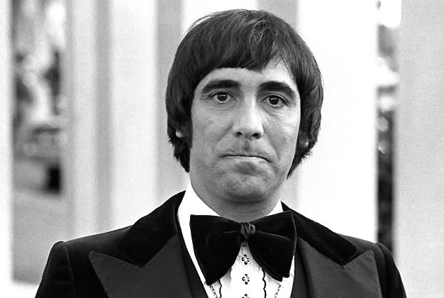 Keith Moon biting his lips with a serious face at the Hollywood Palladium in 1977 while wearing a long sleeve under a bow tie and coat