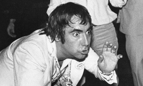 Keith Moon with an angry face and his eyes are wide open while wearing necklace, bracelet, ring, and a long sleeve