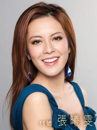 Kelly Cheung smiling while wearing a blue sleeveless blouse and blue earrings