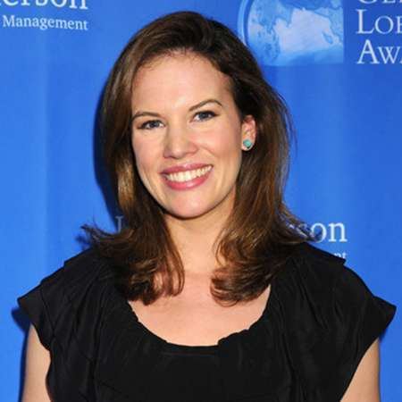 Kelly Evans smiling, with wavy hair, wearing earrings, and a black blouse.