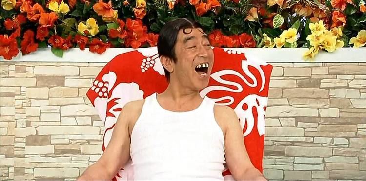 Ken Shimura laughing while wearing false teeth and a white tank top