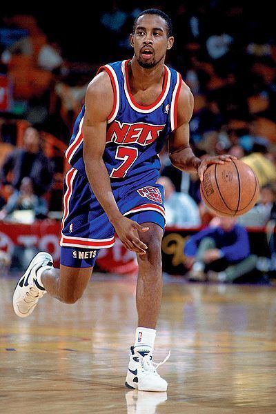 Kenny Anderson at a young age, playing basketball, wearing his basketball uniform, black and white shoes, and white socks.