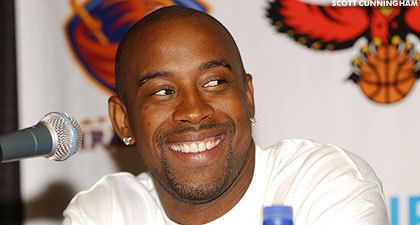 Kenny Anderson wearing a white shirt with a microphone in front of him.