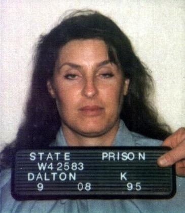 Kerry Lyn Dalton looking serious during her photograph in the State Prison with a board held by a man's hand with the wording, "STATE PRISON W42583 DALTON K 9 08 95". She has black long and curly hair down, wearing a light blue collared top.