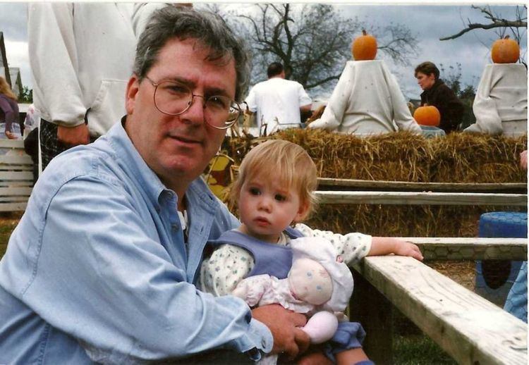 Kevin Cosgrove posing with his daughter in a pumpkin festival wearing sky blue longsleeved shirt.