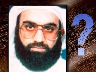 On the left, Khalid Sheikh Mohammed with mustache and beard while wearing eyeglasses, white long sleeves, ghutra, and agal and on the right, is a question mark