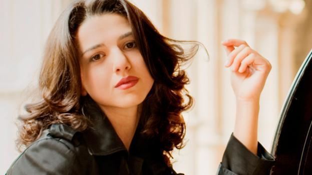 Khatia Buniatishvili posing with her finger in her slightly curled hair and wearing a black coat.