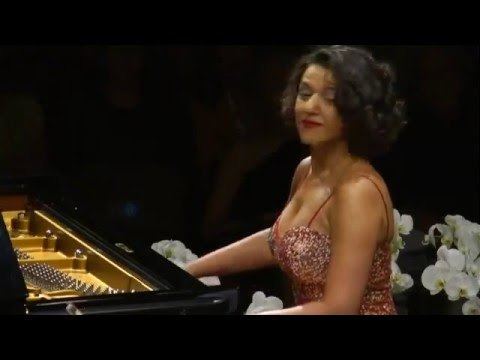 Khatia Buniatishvili playing a a piano on stage and wearing a bejeweled sleeveless dress.