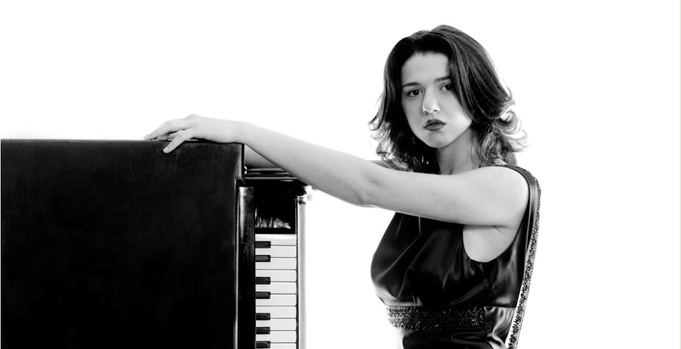 Khatia Buniatishvili posing in a black and white set with a piano and wearing a black sleeveless dress.