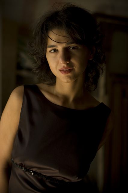 Khatia Buniatishvili half-smiling in a dark room and wearing a black sleeveless dress.