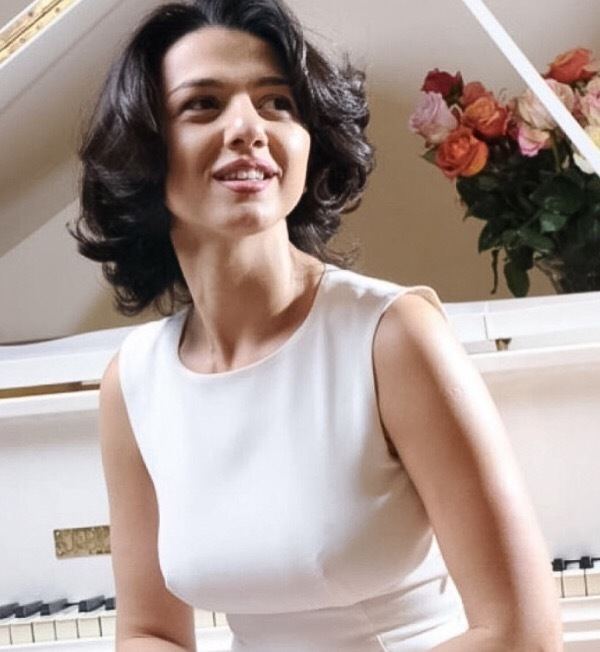 Khatia Buniatishvili smiling and looking at something and wearing a white sleeveless dress.