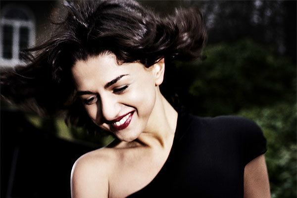 Khatia Buniatishvili smiling with her hair windswept and having red lipstick while wearing a black dress.