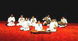 A group of people sitting on the floor while playing Khrueang sai and other instruments while wearing white long sleeves and pants