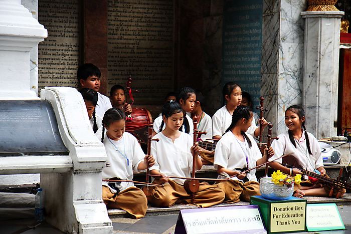 School girls and boys playing khrueang sai in front of a temple while wearing a white shirts and brown pants