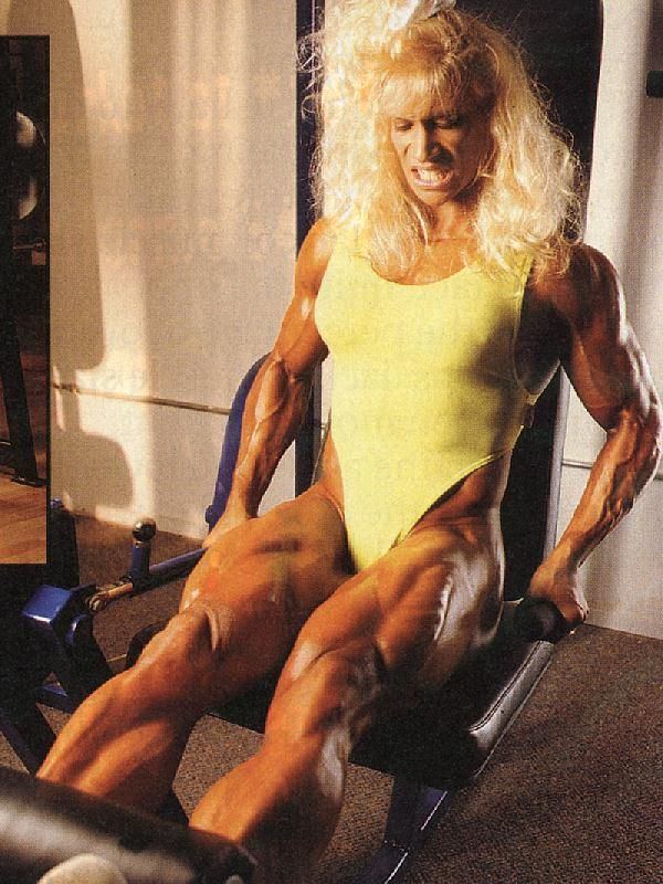 Kim Chizevsky-Nicholls doing leg extention exercise in a leg extension machine and wearing yellow one piece bikini.