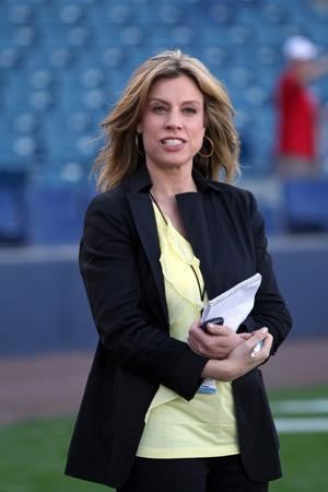 Kim Jones holding a notebook during a football game and wearing a black blazer over a yellow shirt and black pants.
