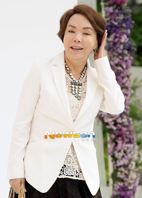 Kim Soo-mi smiling and wearing a necklace and a white blazer while holding her hair.