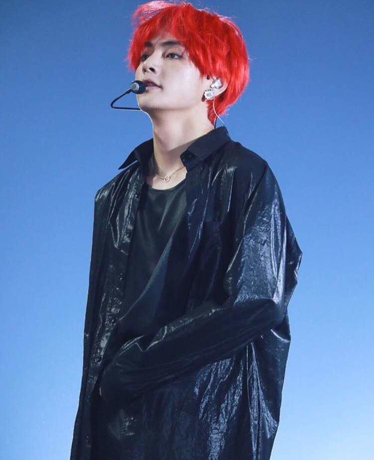 Kim Taehyung with a wired microphone, with color red hair, wearing earrings, a necklace, black long sleeves, a black shirt, and black pants.