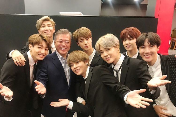 The BTS with the President of South Korea all are smiling and wearing black suits.