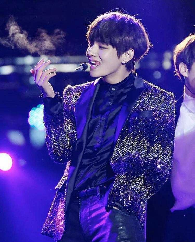 Kim Taehyung performing on stage, with a wired microphone, wearing a fancy coat, black long sleeves, and black pants.