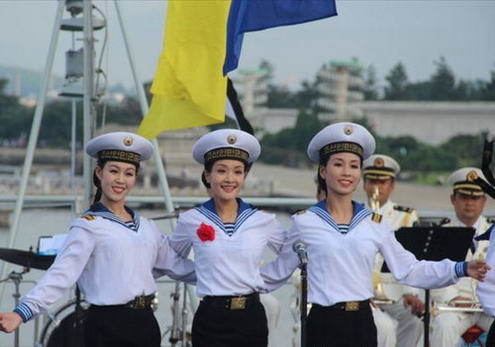 A three North Korean navy female soldiers smiling together while wearing white and blue long sleeves, hat, and black skirt