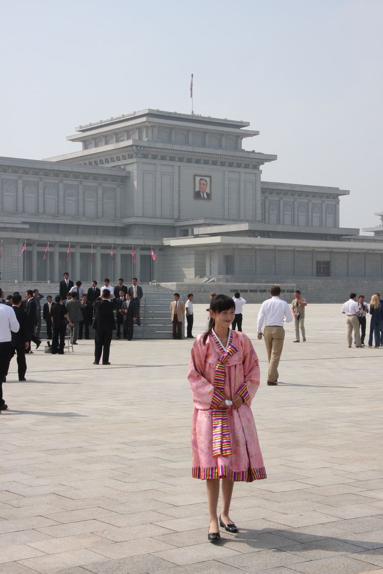Woman standing in front of Kumsusan Memorial Palace while wearing a pink North Korean traditional dress