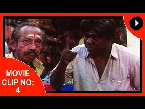 Movie clip starring Krishnankutty Nair with a mustache and wearing a yellow polo shirt with a man wearing a white polo shirt and doing a punch hand gesture.